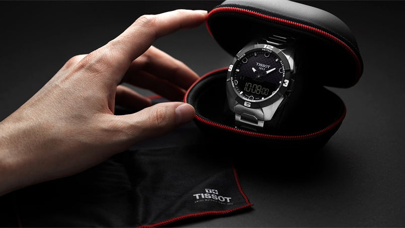 Tissot watch in a black and red case held by a hand on a dark background