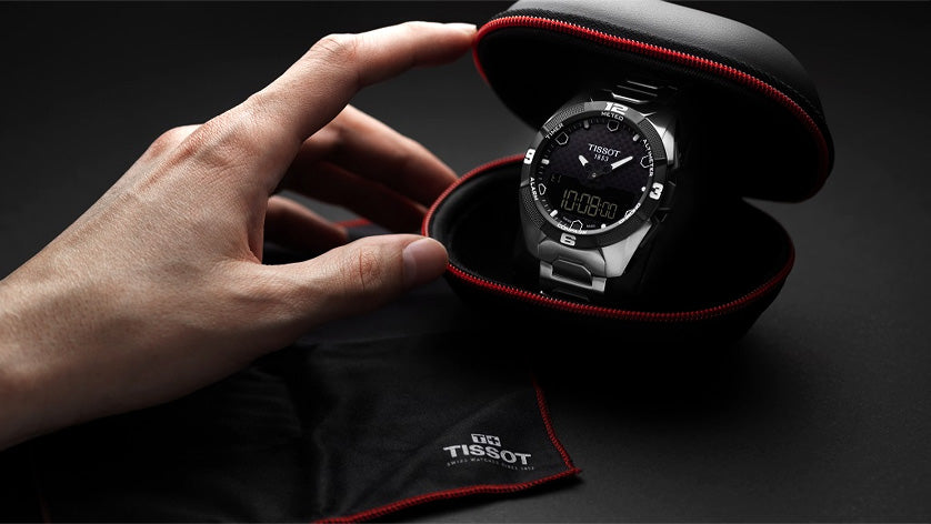 Tissot watch in a black and red case held by a hand on a dark background
